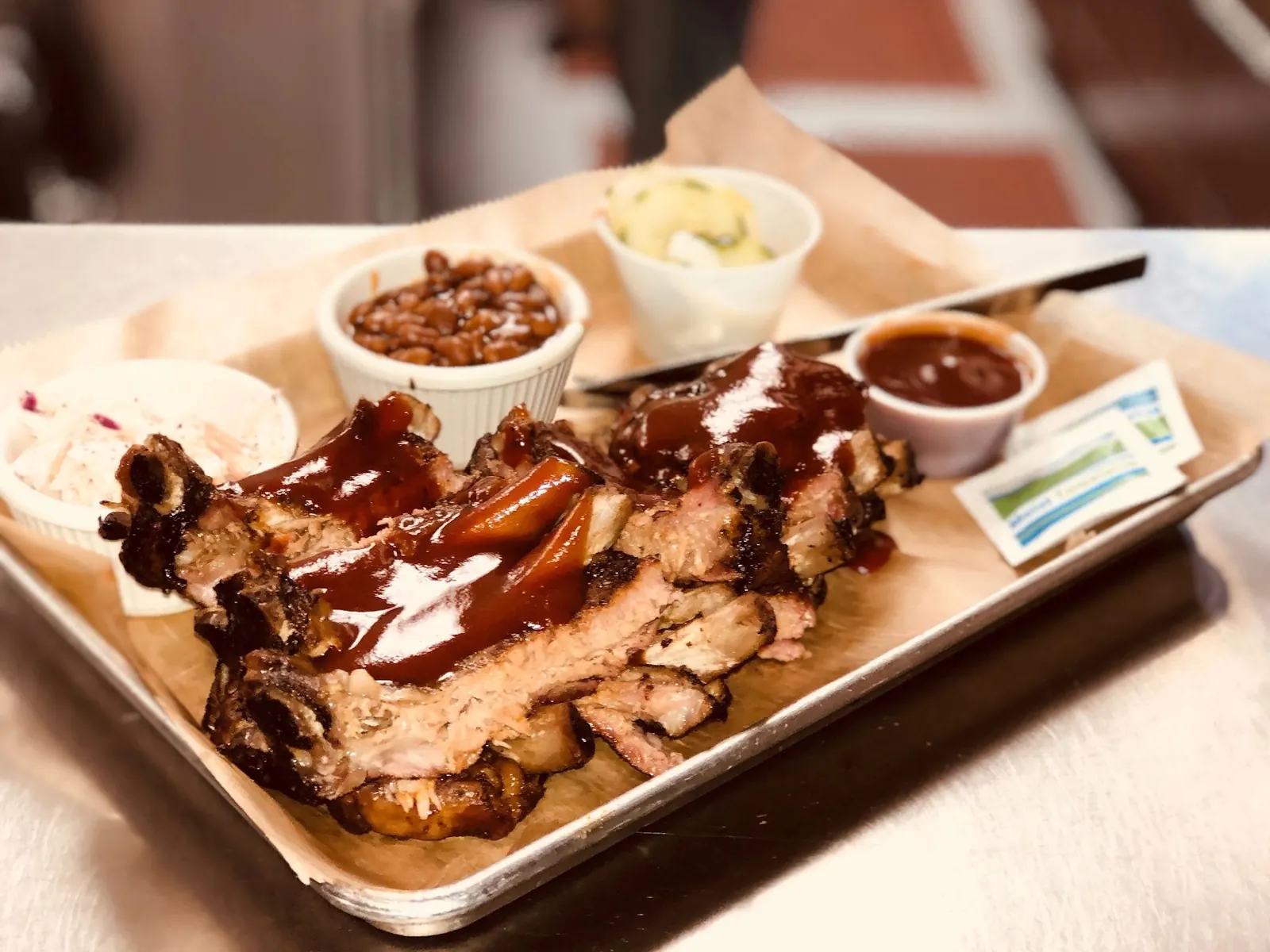 Smoked ribs with house BBQ sauce, baked beans and sides on a tray at The Iron Pig Smokehouse