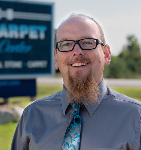 Ken Roberts, owner, smiling in front of the company sign in Northern Michigan
